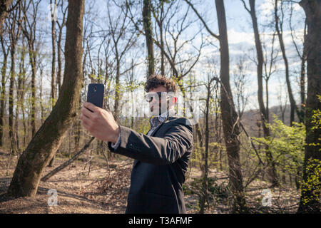 Un giovane uomo bello, parlando un selfie all aperto in natura. Faccia grave espressione, indossando occhiali da sole. Foto Stock