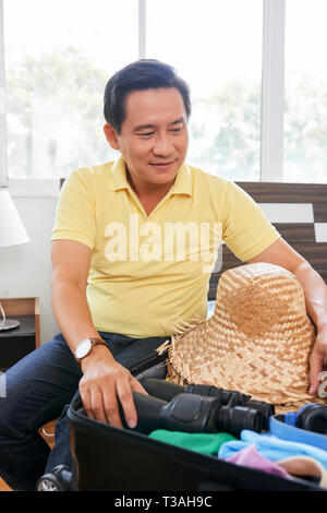 Maturo uomo vietnamita valigia di imballaggio con hat e binocolo Foto Stock
