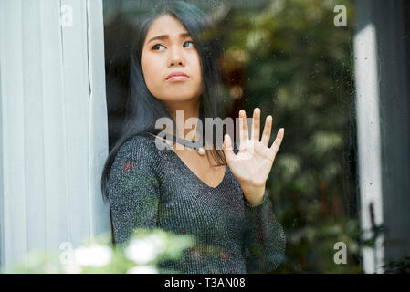 Pensieroso giovane donna guardando attraverso la finestra Foto Stock