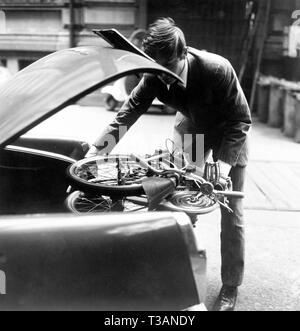 Automobilista mettendo bicicletta pieghevole in tronco, 1965 Foto Stock