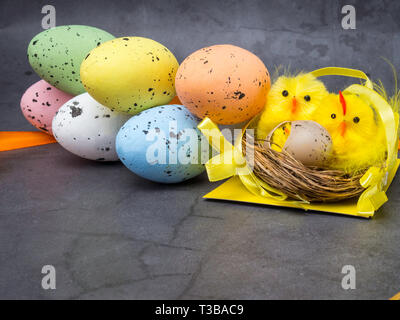 Un simpatico pulcino di Pasqua in un nido circondato da uova colorate, cartolina di pasqua Foto Stock