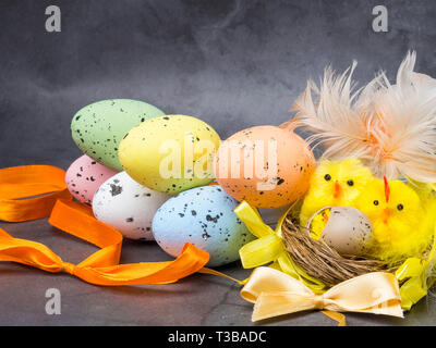 Un simpatico pulcino di Pasqua in un nido circondato da uova colorate, cartolina di pasqua Foto Stock