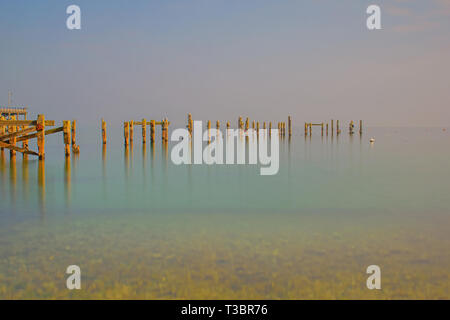 Una lunga esposizione vista ancora,acque calme al vecchio molo Swanage,riflettere splendidamente il weathered pilastri permanente ,golden alla luce Foto Stock