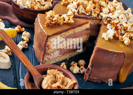 Fette di banana pan di spagna a strati con burro di arachidi mousse e guarnita con glassa al cioccolato fuso caramello e popcorn dolce, vista orizzontale da Foto Stock