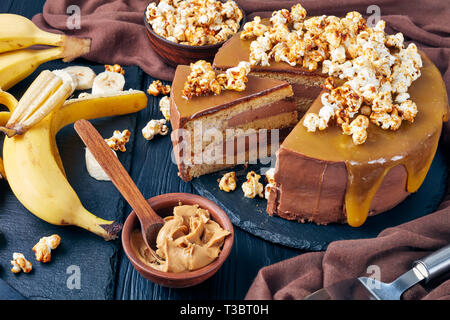 Fette di banana pan di spagna a strati con burro di arachidi mousse e guarnita con glassa al cioccolato fuso caramello e popcorn dolce, vista orizzontale da Foto Stock
