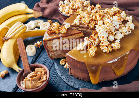 Close-up di una banana a fette di pan di spagna a strati con burro di arachidi mousse e guarnita con glassa al cioccolato fuso caramello e popcorn dolce, Horizon Foto Stock