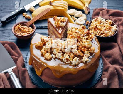 Close-up di una banana a fette di pan di spagna a strati con burro di arachidi mousse e guarnita con glassa al cioccolato fuso caramello e popcorn dolce, Horizon Foto Stock