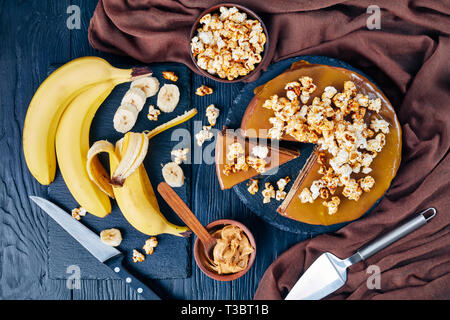 Fette di banana pan di spagna a strati con burro di arachidi mousse e guarnita con glassa al cioccolato fuso caramello e popcorn dolce, vista da sopra, ingr Foto Stock