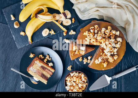 Fette di banana pan di spagna a strati con burro di arachidi mousse e guarnita con glassa al cioccolato fuso caramello e popcorn dolce, vista da sopra, ingr Foto Stock