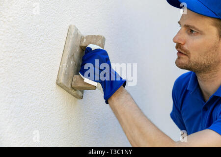 Uomo decorativo applicazione di intonaco di facciata con frattazzo su casa parete esterna Foto Stock