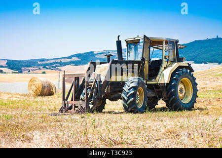 Il vecchio trattore fermo in una collina con balle rotonde sullo sfondo Foto Stock