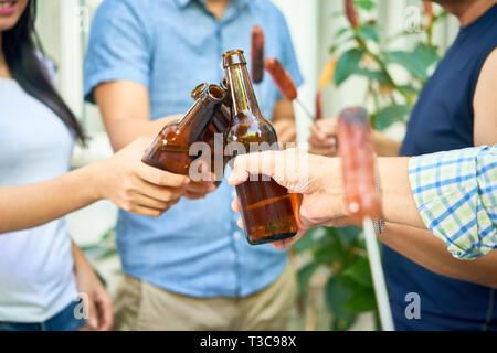Le mani di amici la tostatura con bottiglie di birra quando aventi parti in cortile Foto Stock