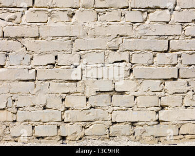 La trama di un vecchio muro di mattoni è dipinta con luce di vernice di colore beige ed è illuminata dalla luce del giorno Foto Stock