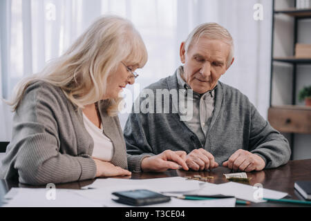 Coppia senior in abiti casual seduta a tavola con scartoffie pur contando il denaro Foto Stock