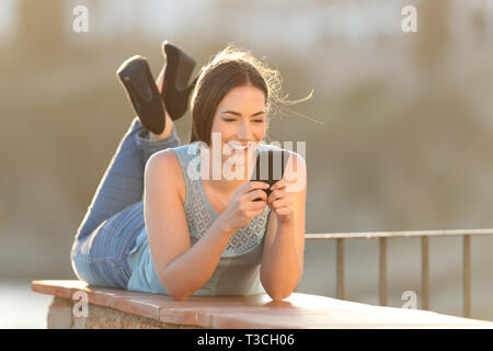 Corpo pieno ritratto di una donna felice utilizzando uno smart phone giacente in un balcone Foto Stock