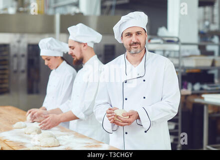 Baker contro lo sfondo dei lavoratori in panetteria. Foto Stock