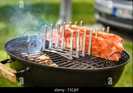 Bimbo indietro costine arrosto su barbecue bollitore barbecue grill. Home reso costolette di maiale alla griglia con una marcia bassa e molto lentamente. La cottura alla griglia all'aperto in natura a fami Foto Stock
