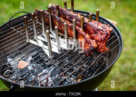 Bimbo indietro costine arrosto su barbecue bollitore barbecue grill. Home reso costolette di maiale alla griglia con una marcia bassa e molto lentamente. La cottura alla griglia all'aperto in natura a fami Foto Stock