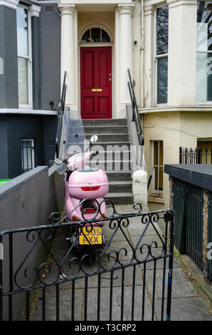 Una rosa scooter è parcheggiato su un percorso di giardino nella parte anteriore dei gradini che portano fino a una porta anteriore in una casa a Londra/ Foto Stock