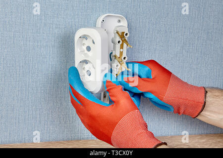 Chiusura del cambio scatola da incasso della presa di corrente a muro da elettricista in guanti di protezione. Foto Stock