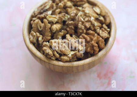 I kernel di noci pelate i dadi in una ciotola di legno su uno sfondo rosa, concetto di mangiare sano cibo vegan. Close up, il fuoco selettivo, copia dello spazio. Foto Stock