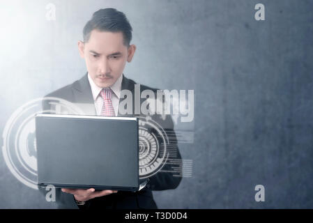 Attraente imprenditore asiatica guardando il laptop con schermo virtuale che visualizza l'interfaccia di mappa del mondo e il codice binario sulla parete dello sfondo. Foto Stock