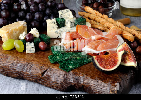 Piatti per antipasto su una tavola di legno con prosciutto, diversi tipi di formaggio, uva e fichi Foto Stock