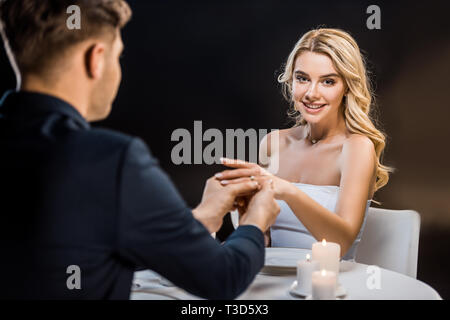 Giovane sposo di mettere l'anello di matrimonio su brides dito su sfondo nero Foto Stock