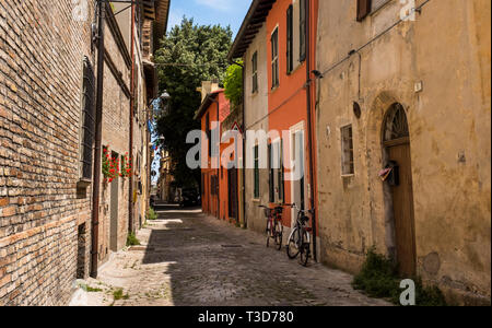 Scena colorata di una tranquilla, stretta strada di ciottoli, case e biciclette di Fano, Italia Foto Stock