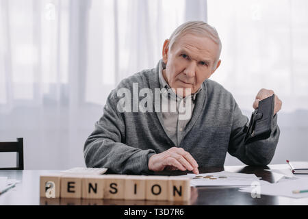 Titolare di pensione o di rendita maschio con portafogli e documenti seduta a tavola con la parola 'pensione" fatta di blocchi di legno in primo piano Foto Stock