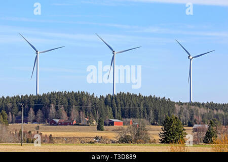 Fila di tre turbine eoliche paese vicino villaggio nel sud della Finlandia in una giornata di sole di primavera. Foto Stock