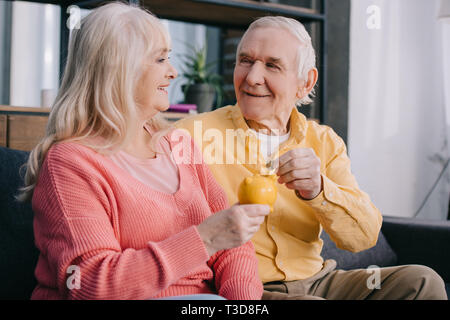 Felice coppia senior mettendo coin in giallo salvadanaio Foto Stock