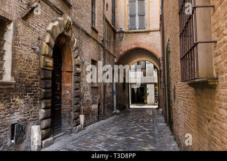 Street view lungo uno stretto passaggio di ciottoli che passa attraverso un edificio arcuato di Fano, Italia Foto Stock