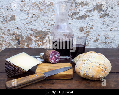 Un maiale iberico insaccato su una vecchia tavola di legno con un cuneo di formaggio di pecora, un coltello di antiquariato e una bottiglia e un bicchiere di rosso vino spagnolo Foto Stock