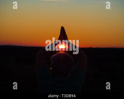 Un senior donna pratica lo yoga al tramonto Foto Stock