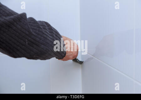 Il lavoratore la riparazione di installatore sulla parete con cazzuola, rimuove il silicone bianco per la posa di piastrelle di finitura. Foto Stock