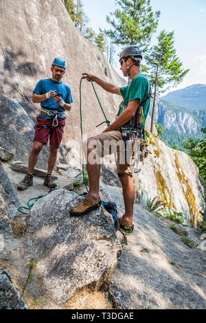 Un uomo di consegnare la corda di arrampicata al suo partner di arrampicata prima di avviare un percorso di arrampicata. La poco fumo Bluffs, Squamish, BC, Canada. Foto Stock