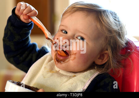 Baby girl alimentare se stessa con il cioccolato sul suo viso Foto Stock