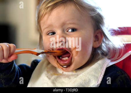 Baby girl alimentare se stessa con il cioccolato sul suo viso Foto Stock