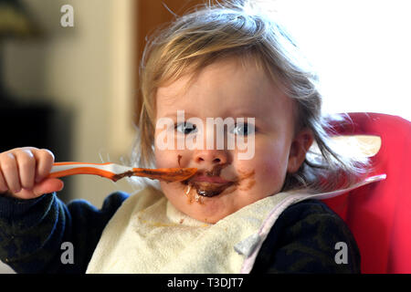 Baby girl alimentare se stessa con il cioccolato sul suo viso Foto Stock