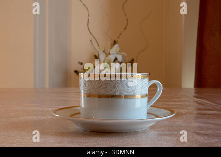 Bone China oro bordata tea coffee cup con piastra di colore bianco crema con fiori in background indoor Foto Stock