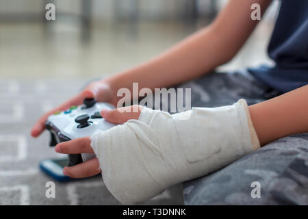 Bambino con braccio rotto utilizzando video controller di gioco Foto Stock