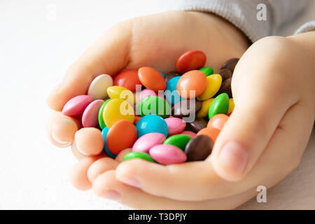 Round, multicolore e cioccolatini. Close-up. Un mucchio di multi-caramelle colorate. Un bambino tiene una caramella. Foto Stock