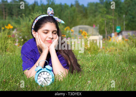 Ragazza triste con la sveglia nel giardino estivo Foto Stock