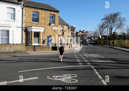 Vista posteriore di una giovane donna che indossa la lycra che corre lungo Pulross Rd all angolo della strada Dalyell case in Brixton a sud di Londra Inghilterra REGNO UNITO KATHY DEWITT Foto Stock