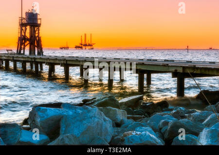 Il sole sorge alle spalle di un gas naturale rig e una torre meteo azionato dal NOAA Dati nazionali Centro boa in Dauphin Island, Alabama. Foto Stock