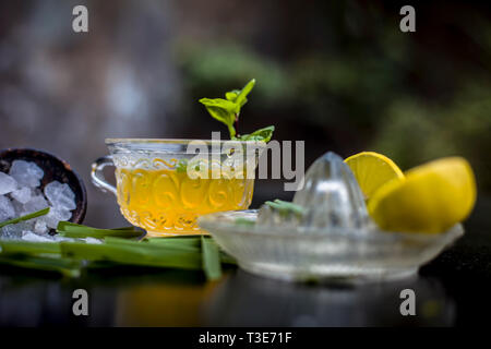 Close up ghiacciata di erba di limone tè in una coppa trasparente su una superficie di legno con materie di erba di limone Tè verde in una tazza e lo zucchero in un recipiente di argilla con il cubo del ghiaccio Foto Stock