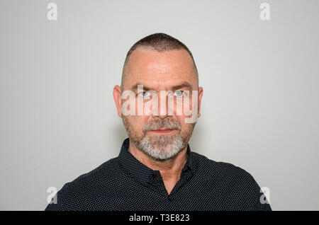 Grave elegante uomo di mezza età con un espressione pensosa fissando direttamente alla fotocamera in una testa e la spalla verticale su un grigio di sfondo per studio Foto Stock