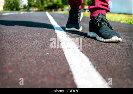 Un bambino in sneakers passeggiate lungo la linea bianca in corrispondenza della via di corsa su un giorno d'estate. Effettuare la scelta, del mezzo di trasporto che attraversa la frontiera. Concetto di restrizione. Copia dello spazio. Foto Stock