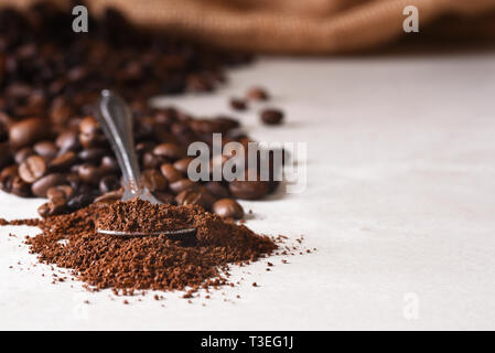 Primo piano di un cucchiaio di caffè macinato con fagioli whoel fuoriuscita di un sacco di tela in background. Profondità di campo. Foto Stock